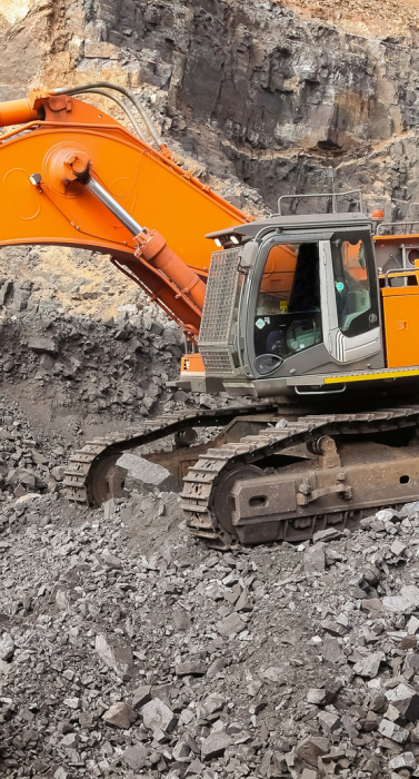 A yellow excavator digging for ore rich rock in an open pit mine